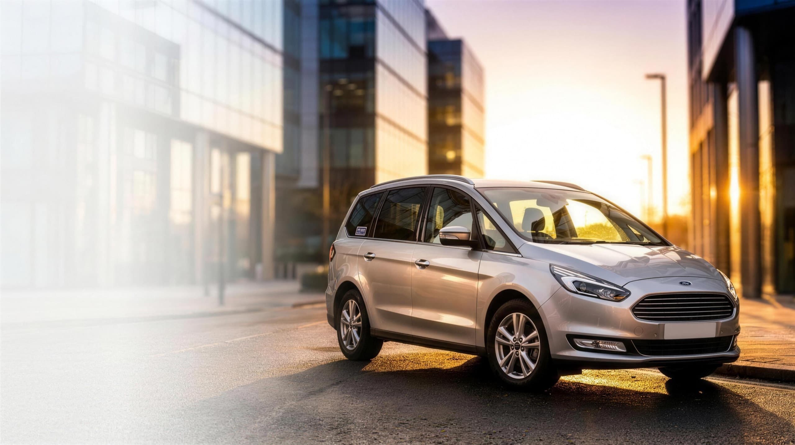 A silver Ford Galaxy seven-seat MPV private-hire car on a golden-hour city street